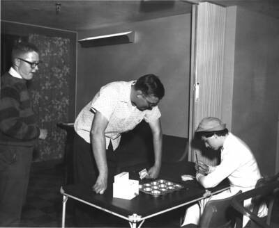 Two men donate money to the Ethel Steel House at the Nickel Hop. One woman collects money and fills out raffle tickets.