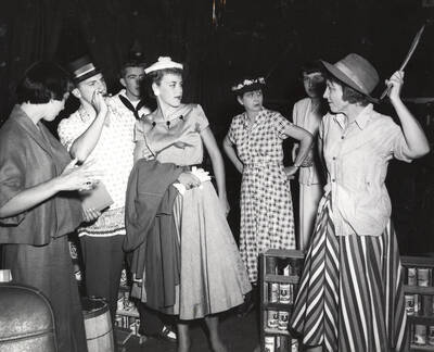 Directed by Cecil Matson for Summer Theatre in the Field House. A group of people looking at a woman holding something in the air in 'Suds in Your Eye."