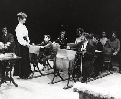 Directed by Don Hill. A woman standing in front of a group of people sitting in desks. Summer Theatre in the Field House directed by Donald Hill.