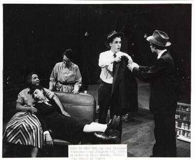 Summer Theatre in the Field House directed by Cecil Matson. A woman holding a sleeping woman on the couch. Another woman looking at the sleeping woman from behind the couch. Two men holding a coat facing each other.
