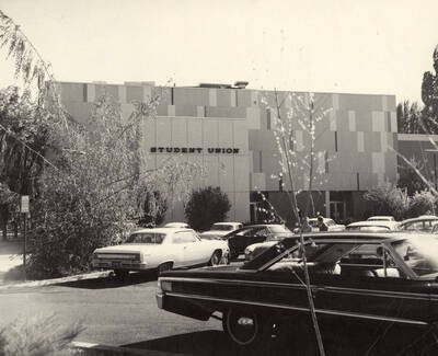 Cars are parked in the parking lot with the Student Union Building in the background.