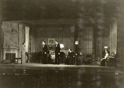 During the drama production of "Dangerous Corner," men and women stand on stage facing one woman. Cast: Robert Herrick as Gordon Whitehouse, Dorothy Pierce as Freda Chatfield, Eldred Stephenson as Robert Chatfield, Alline King as Olwen Peel, Paul Selby as Charles Stanton, Nina Varian as Betty Whitehouse, Ethlyn O'Neal as Maud Mockridge.  Directed by Fred Blanchard.