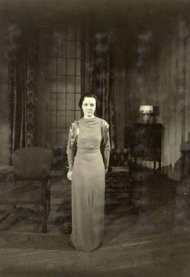 During the drama production of "Dangerous Corner," a woman stands for a picture. Cast: Robert Herrick as Gordon Whitehouse, Dorothy Pierce as Freda Chatfield, Eldred Stephenson as Robert Chatfield, Alline King as Olwen Peel, Paul Selby as Charles Stanton, Nina Varian as Betty Whitehouse, Ethlyn O'Neal as Maud Mockridge. Directed by Fred Blanchard.