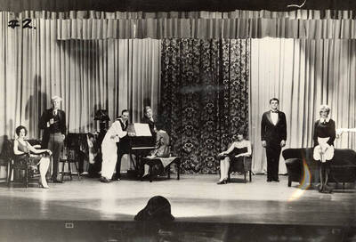 Men and women hang out around a piano as a woman plays during the drama production of "Fourteen," written by Talbot Jenning, directed by Lillian Woodworth for Advanced class.