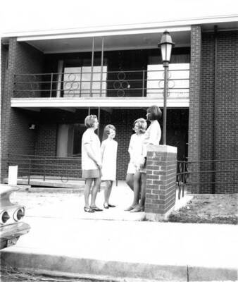 Four women stand outside the Alpha Gamma Delta house, located at 727 Nez Perce Drive, 1967 or later.