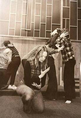 Women face away as one woman kneels during a drama production.