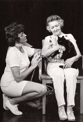 Two women sit on stage holding a cat during a drama production. The cat is trying out for a role in  Summer Theatre's 'Gigi' in the Field House.