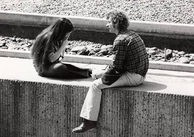 A man and woman sit near the water feature in the Library Plaza rehearsing.