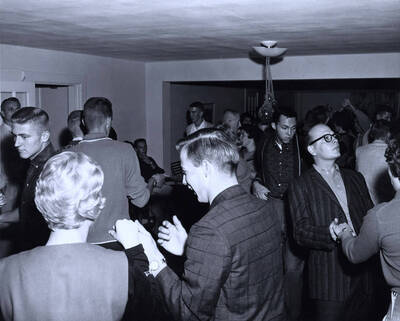 Students dance at the Delta Gamma Nickel Hop. Two men taking a break can be seen sitting down in the background.