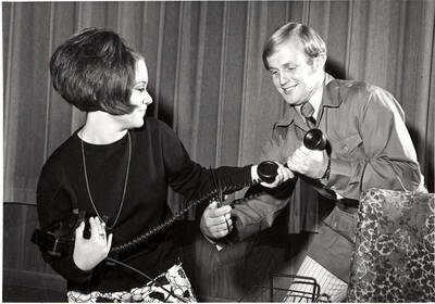 Scene from the University of Idaho production of "The Telephone." Two actors can be seen holding a phone, while one of them is cutting the cord with scissors.
