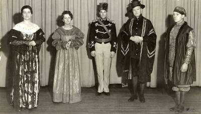 Group scene from the University of Idaho drama production of "The Gondoliers." The cast members can be seen dressed in costume and standing on stage. Pictured from left to right are Alice Bell, Ruth Johnson, Wayne Hampton, Jenkin Palmer and Robert Harris.