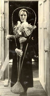 Scene from the University of Idaho drama production of "Torch Bearers." Directed by Fred Blanchard, Technical Director Theodore Prichard. A woman can be seen dressed in costume and holding flowers. Members of the cast include Catherine Brandt as Mrs. J. Duro Pampinelli, Grace Eldridge as Mrs. Nelly Fell, Marthalene Tanner as Mrs. Paula Ritter and Leland Cannon as Fred Ritter.