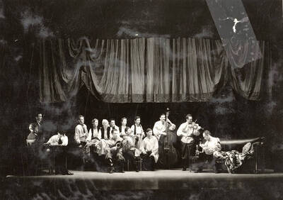 Scene from the University of Idaho drama production of "The Living Corpse." Directed by Fred Blanchard, Technical Director Theodore Prichard. Actors can be seen on stage, holding musical instruments. Cast members include Fred C. Blanchard as Fedya, Ethlyn O'Neal as Lisa, Clayne Robison as Victor, Alberta Bergh Utt as Masha, Raphael Gibbs as Prince Sergius, Erma Lewis as Anna Pavlovna, Casady Taylor as Petrovitch, Earl Bopp as Artimiev, and Joe Paquet as Petushkov.