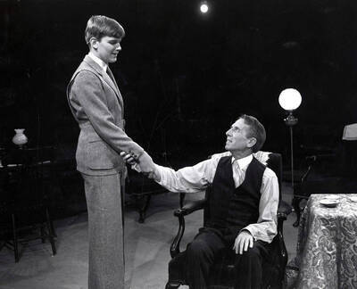 Scene during the University of Idaho drama production of "Ah, Wilderness." Directed by Forrest Sears for Summer Theatre in the Field House.Bill Byrd (right) is sitting in a chair, shaking the hand of another actor.