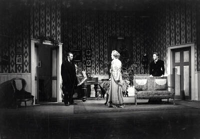 Scene from the University of Idaho drama production of "A Doll's House." ASUI production was directed by Jean Collette. Two men and a woman can be seen on stage talking with each other.