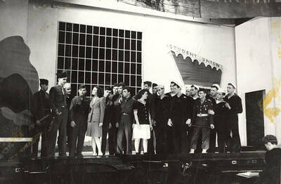 Scene from the ASUI production of "Gee-Eyes Right." Members of the cast can be seen standing on stage under a sign that says 'Student Union'. Directed by Jean Collette, written Ted Sherman and Geoffrey Cope, music by Hall Macklin, costume advisor Marion Featherstone.