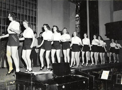 Scene from the ASUI production of "Gee-Eyes Right." A group of women are wearing matching costumes and seem to be dancing. Directed by Jean Collette, written Ted Sherman and Geoffrey Cope, music by Hall Macklin, costume advisor Marion Featherstone.