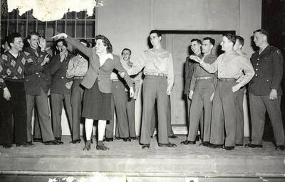 Scene from the ASUI production of "Gee-Eyes Right." Three cast members can be seen talking, while others look on. Directed by Jean Collette, written Ted Sherman and Geoffrey Cope, music by Hall Macklin, costume advisor Marion Featherstone.