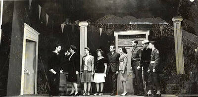 Scene from the ASUI production of "Gee-Eyes Right." Members of the cast can be seen standing on stage in costume, watching as a man and woman have a conversation with each other. Directed by Jean Collette, written Ted Sherman and Geoffrey Cope, music by Hall Macklin, costume advisor Marion Featherstone.