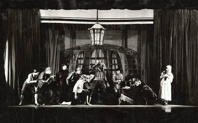 Scene from the drama production of "The Bell Tolls Three" revised by Talbot Jennings. A man holds a knife above his head, while others look on. Part of a series of One-Act Plays dir by John H. Cushman in the U-Hut theatre, produced by Little Theatre Class.