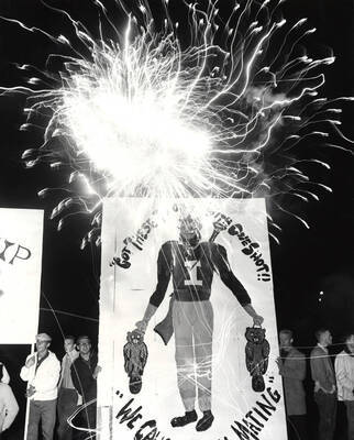 Students holding a sign showing Joe Vandal holding beavers in his hands during the fireworks display at the Homecoming rally and bonfire.