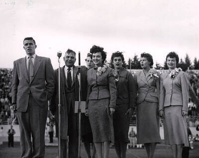 Philip Kleffner, F.L. Bloomquist, Clara Armstrong and other Homecoming royalty stand on a stage during halftime during the University of Idaho vs. San Jose State football game. Pictured left to right: Philip Kleffner (ASUI president), F.L. Bloomquist (Alumni Association President) and Homecoming queen, Clara Armstrong. Attendants in second row: Sonia Henriksson, Carol Ann Zapp, Lou Ann Olson, and Freda Payne.