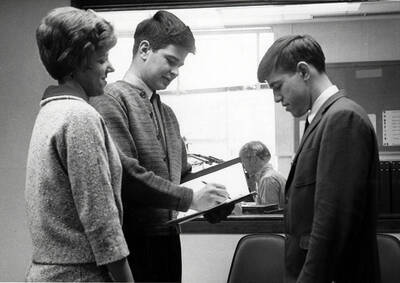 The managing staff of Idaho's KUOI radio station talk while a man in the background speaks into a microphone.
