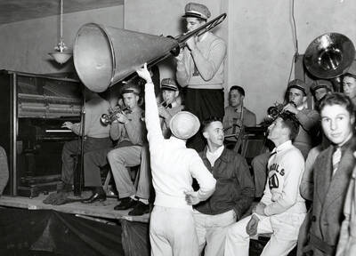 A student plays a trombone while another holds a megaphone up to the instrument during the Idaho pep band's rally.