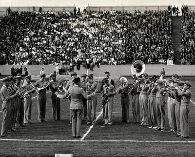 The Idaho pep band plays in a small semi-circle with a crowd full of cheering students in the background.