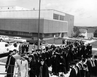 The Idaho commencement procession walks in a line into the Memorial Gym. The library can be seen behind the graduates, with a photographer standing atop it.