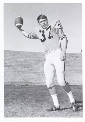 Flanker Don Almquist poses, gripping a football in his right hand.