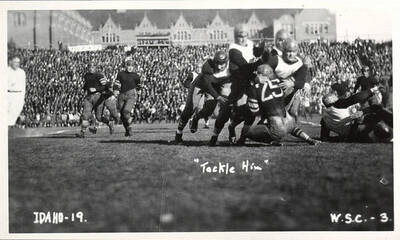A Cougar runner is gang-tackled by a host of Vandals. Caption reads 'Idaho-19, 'Tackle Him',  W.S.C.-3.'