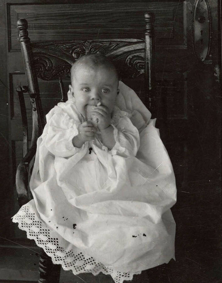 A photograph of an unknown baby sitting and eating.