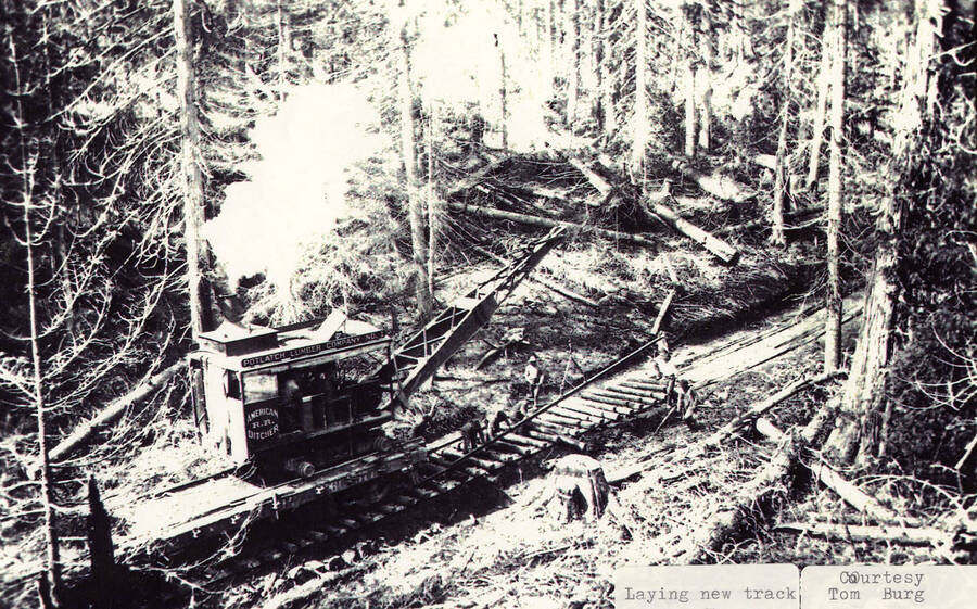 View of men laying new track on one of the railroads. A piece of equipment can be seen on the tracks behind them.