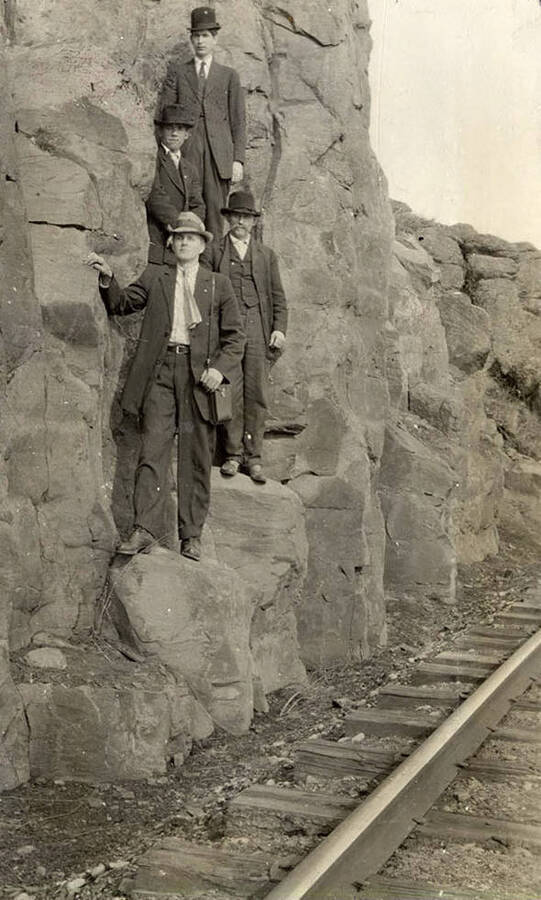 A photograph of four men on rocks next to railroad tracks.