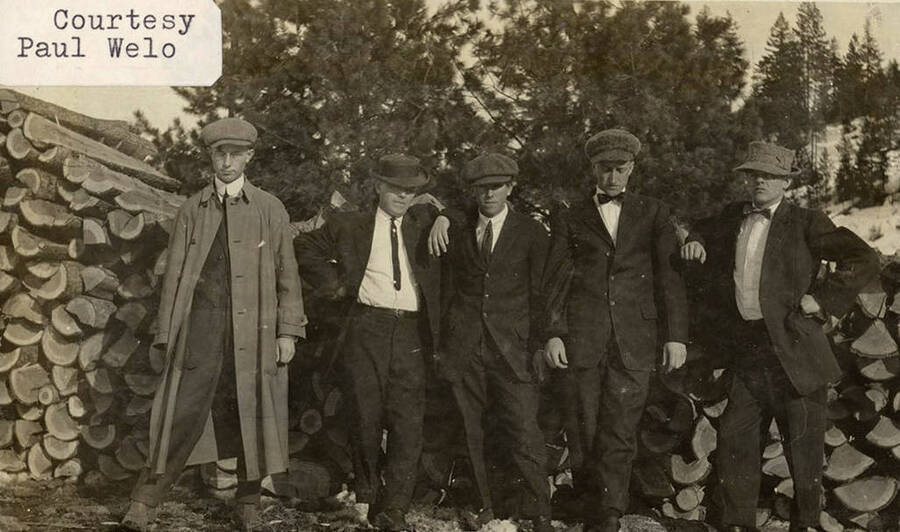 A photograph of five men in front of chopped wood.