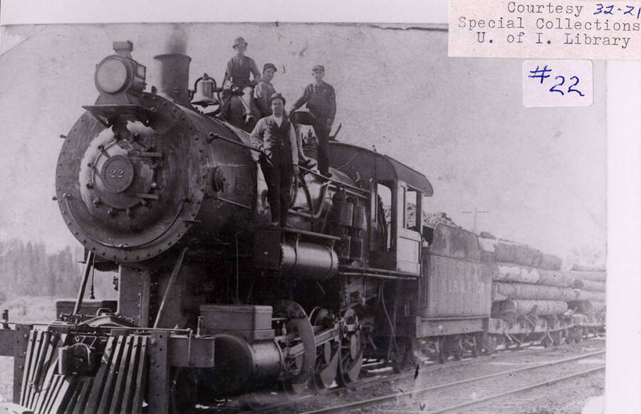 A No. 22 locomotive that is hauling stacks of logs for Potlatch Lumber Company. Four men can be seen standing and sitting on top of the locomotive.