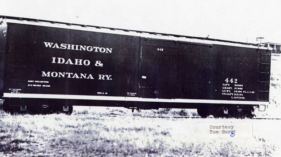 View of a railroad car sitting on the railroad tracks. On the side of the car, it says 'Washington Idaho & Montana Ry'.