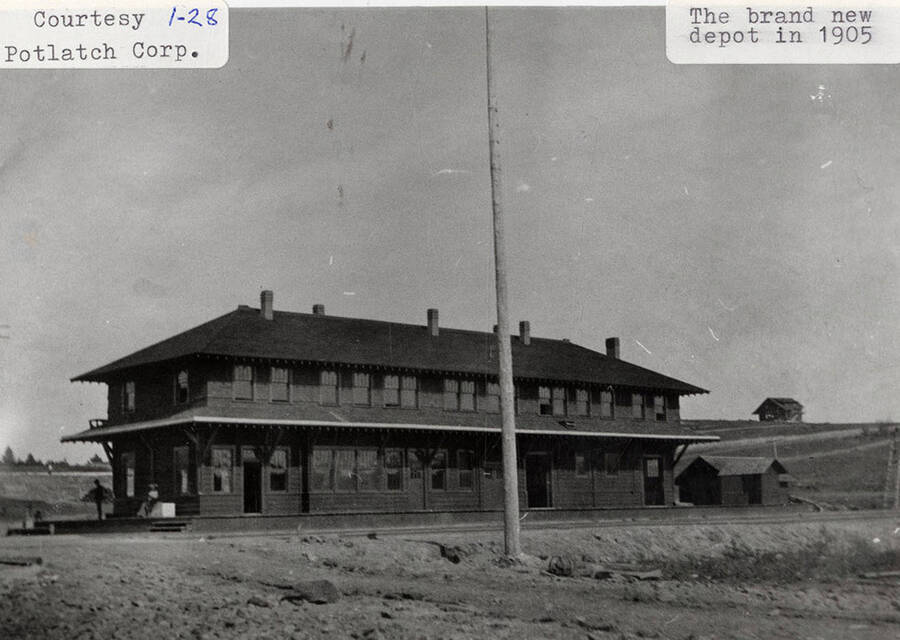 View of the new depot that was built for the railroad. A few people can be seen sitting on the porch of the new building.