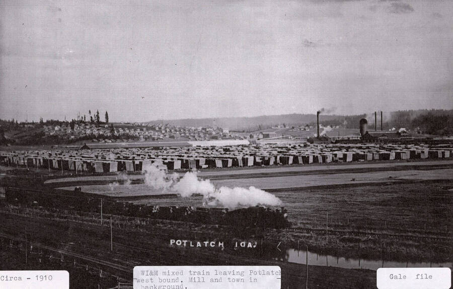 View of a WI&M mixed train leaving Potlatch going west bound. The mill and the town can be seen in eh background.