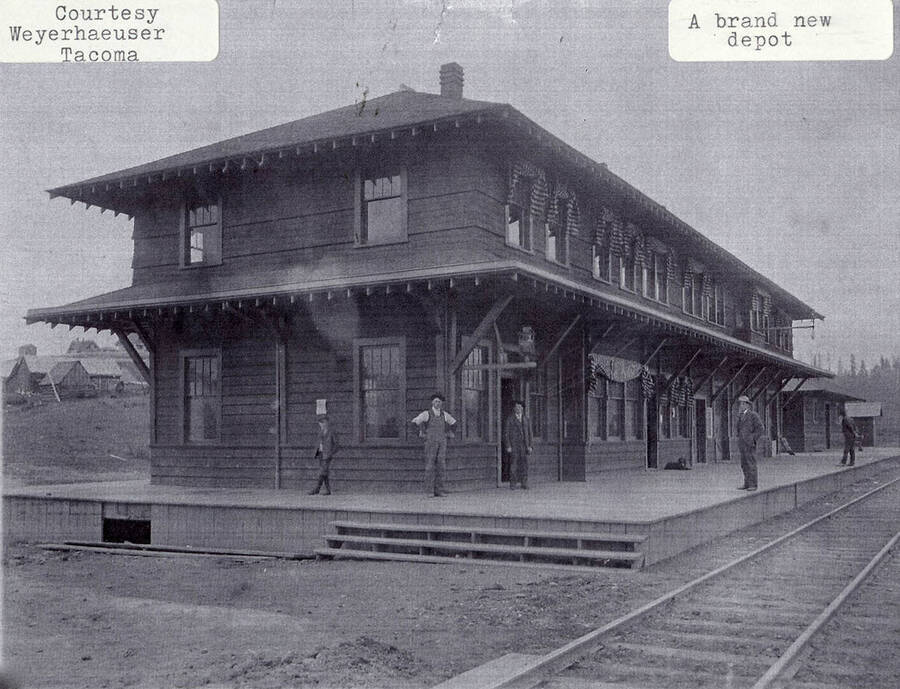 The brand new depot. People can be seen standing on the seck of the new building and curtains can be seen hanging from the windows.