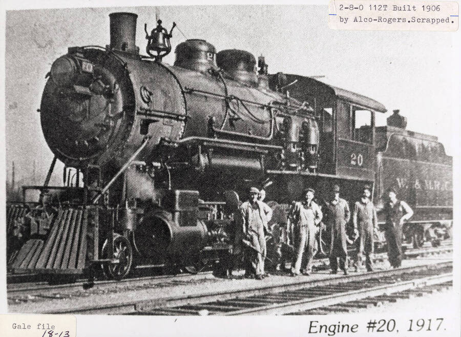 View of a No. 20 locomotive that was built in 1906 by Alco-Rogers. A few men can be seen standing next to the locomotive.