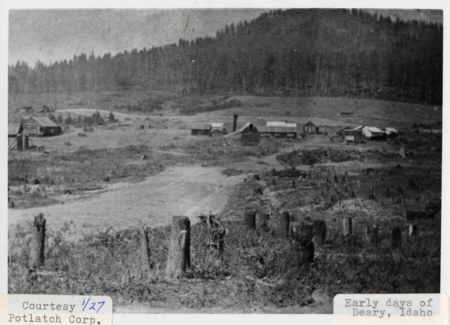 View of Deary, Idaho in the early days. A few buildings can be seen around the town and a hill can be seen in the background.