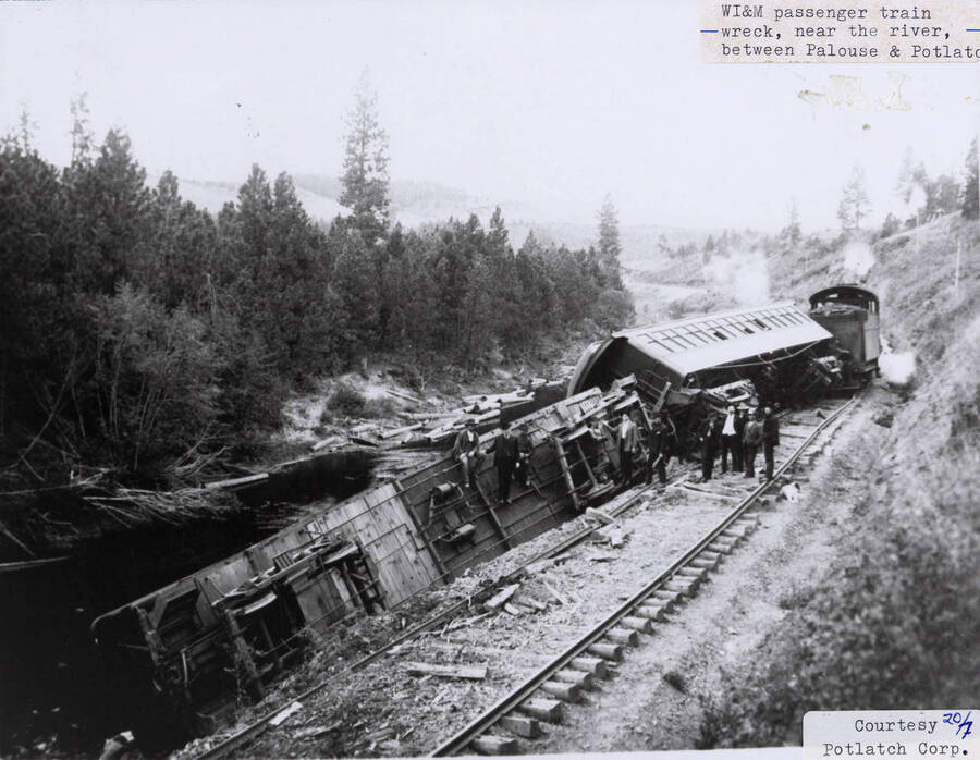 View of a WI&M passenger train wreck near the river between Palouse and Potlatch. Men can be seen standing next to and sitting on top of the train.