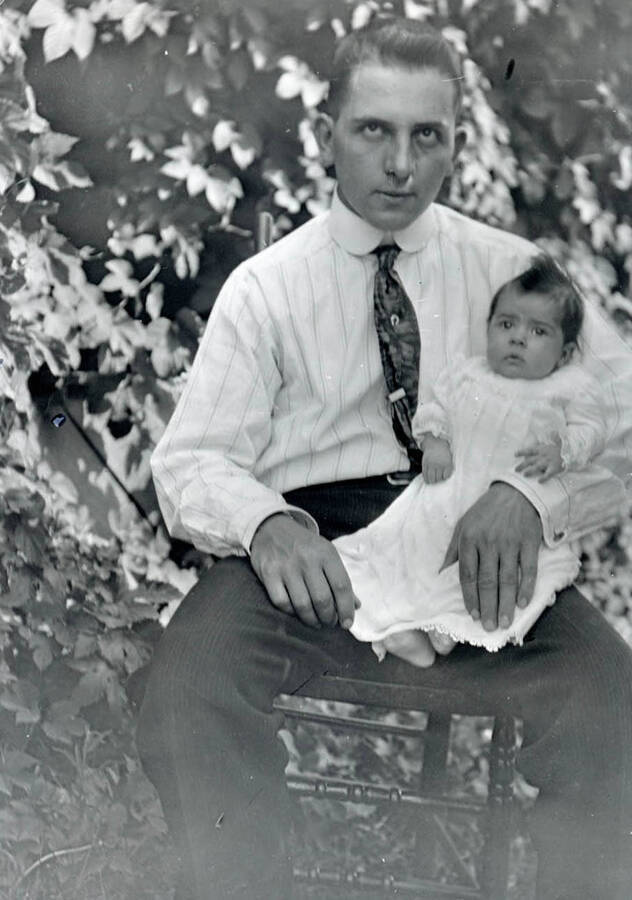 Durrell Nirk sits with his daughter Cleora Anna in his lap in a chair outside.