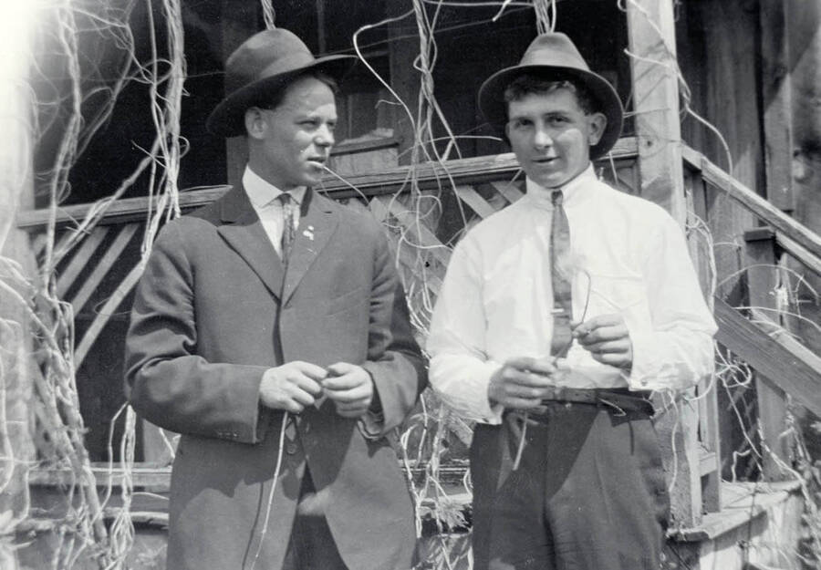 Arthur Strong and Durell Nirk stand wearing hats in front of a house.