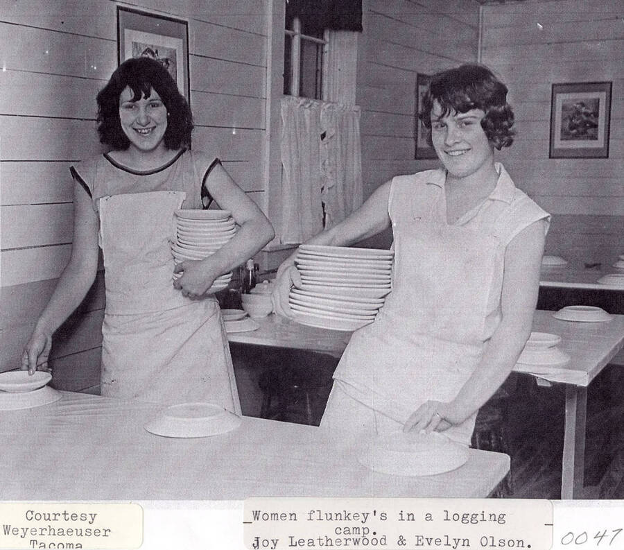 Joy Leatherwood and Evelyn Olson working at a logging camp. The women can be seen placing dishes on tables.