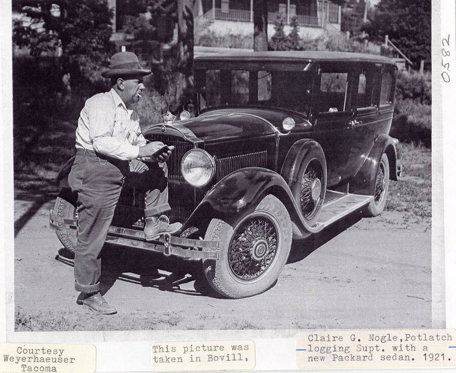 Claire G. Nogle, the Potlatch logging superintendent, leaning on a new Packard sedan. He can be seen writing in a notebook while smoking a cigarette.