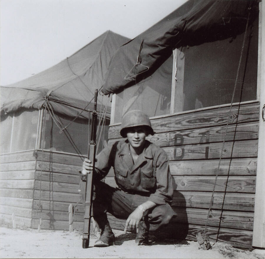 Norman Soncarty poseing with a rifle next to the army barracks in Korea.