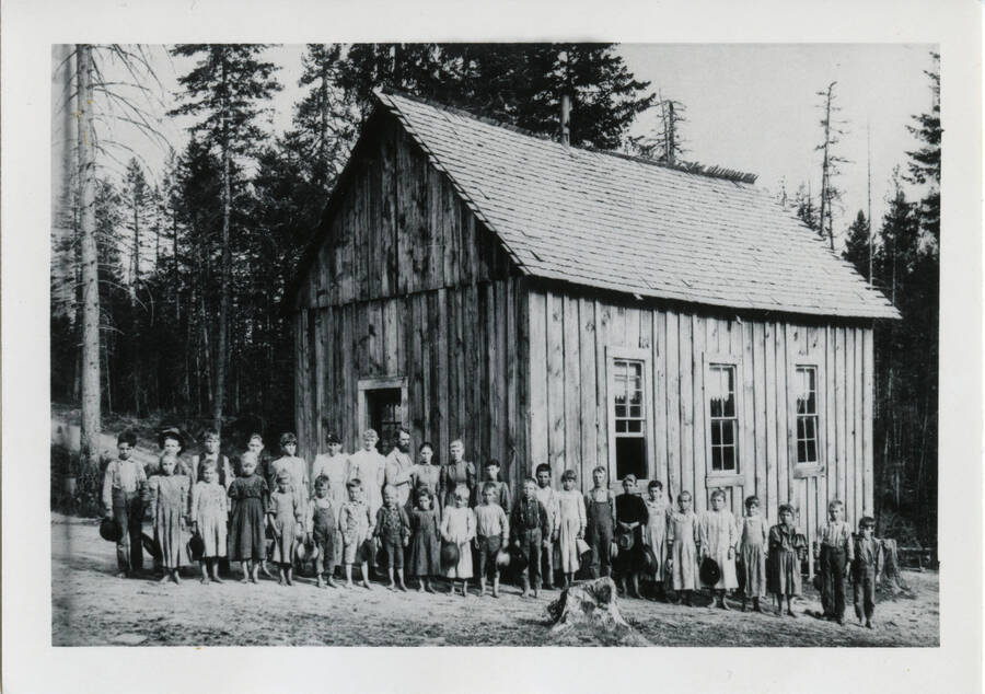 Photo of schoolchildren in front of the schoolhouse, with trees in background